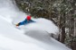 A skier carving hard and creating a cloud of snow.